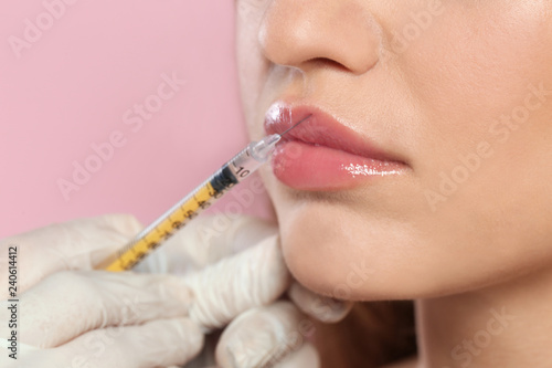 Young woman getting lips injection on color background, closeup. Cosmetic surgery