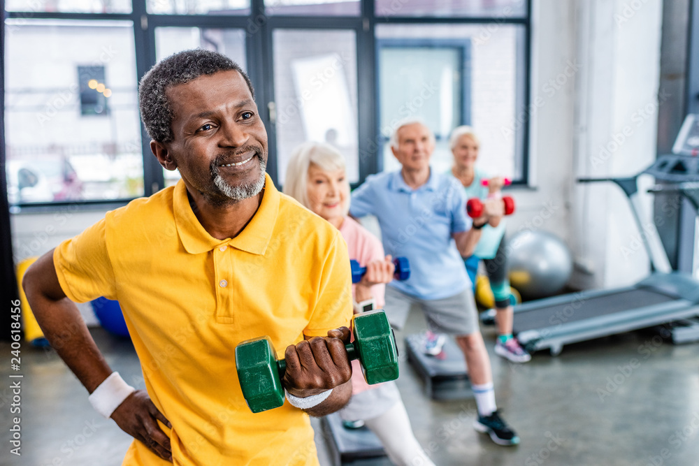 african american man and his friends synchronous exercising with dumbbells at sports hall african american man and his friends synchronous exercising with dumbbells at sports hall