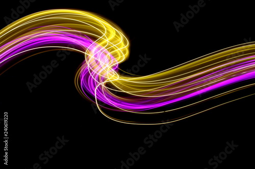 Long exposure, light painting photography. Pink and gold neon streaks of vibrant color against a black background 