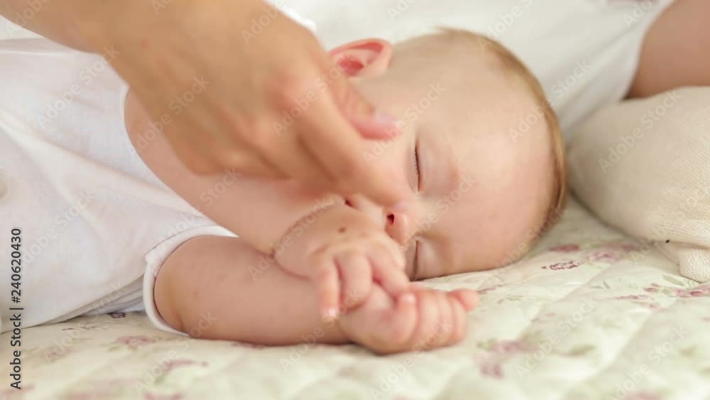 Mom and her newborn baby are sleeping in the bed in the bedroom. Portrait of newborn baby sleeping in bed. Mom gently stroking the baby's hand. Close-up. Mom and her newborn baby are sleeping in the bed in the bedroom. Portrait of newborn baby sleeping in bed. Mom gently stroking the baby's hand. Close-up.