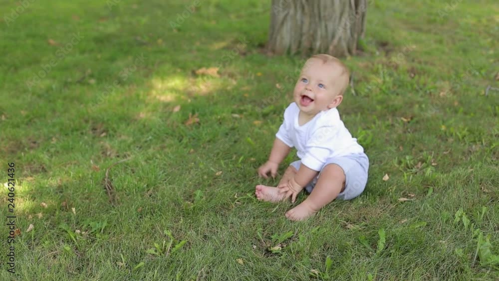Portrait of a five-month newborn baby in the park in the summer, he sits on the green grass and clumsily falls to his side. Portrait of a five-month newborn baby in the park in the summer, he sits on the green grass and clumsily falls to his side.