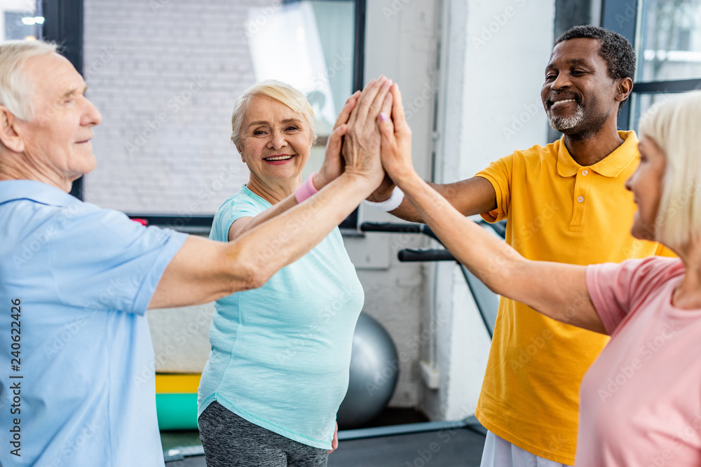 Obraz premium smiling multicultural senior athletes stacking hands together at gym