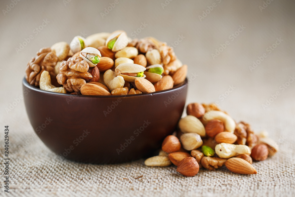 Mix of different nuts in a wooden cup against the background of fabric from burlap. Nuts as structure and background, macro. Top view. Mix of different nuts in a wooden cup against the background of fabric from burlap. Nuts as structure and background, macro. Top view.