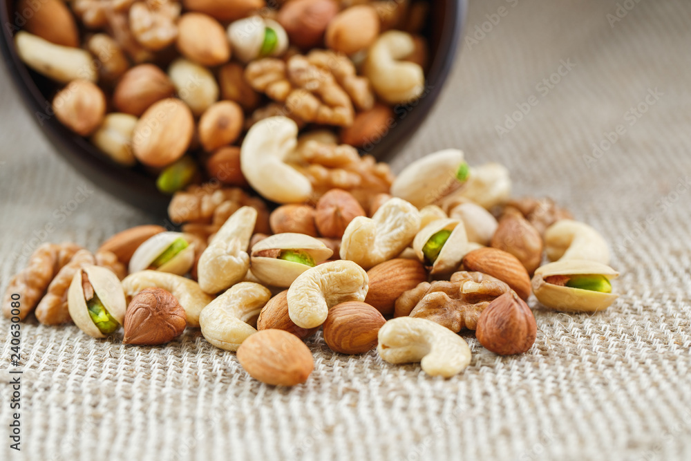 Mix of different nuts in a wooden cup against the background of fabric from burlap. Nuts as structure and background, macro. Top view. Mix of different nuts in a wooden cup against the background of fabric from burlap. Nuts as structure and background, macro. Top view.