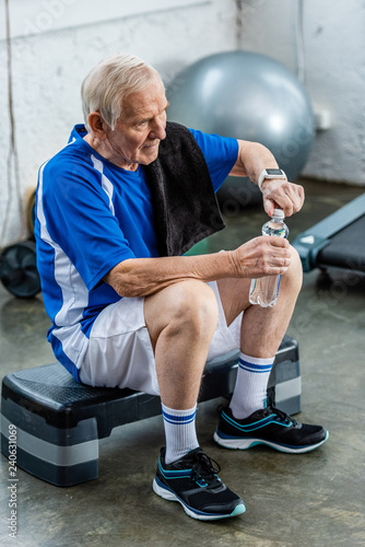high angle view of senior sportsman with towel opening bottle of water resting at gym