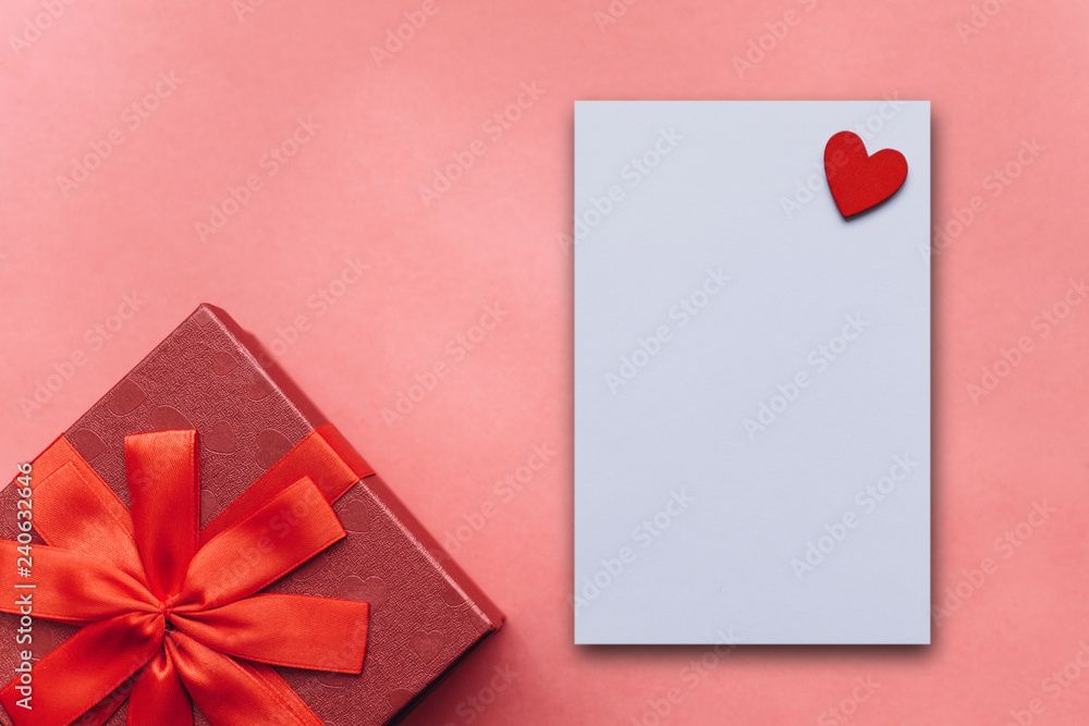 Red box with a gift and next to a white blank sheet for text with a heart on a red background. Festive concept for Valentine's Day or Women's Day or Mother's Day. Red box with a gift and next to a white blank sheet for text with a heart on a red background. Festive concept for Valentine's Day or Women's Day or Mother's Day.
