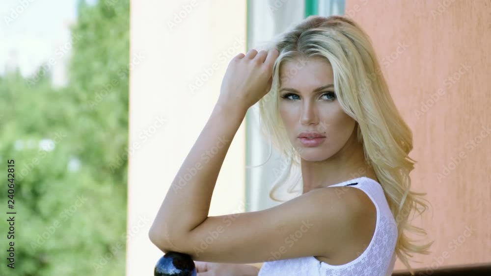 Portrait of attractive smiling young woman posing at camera on sunny summer day on the balcony of luxurious house. 4K Portrait of attractive smiling young woman posing at camera on sunny summer day on the balcony of luxurious house. 4K
