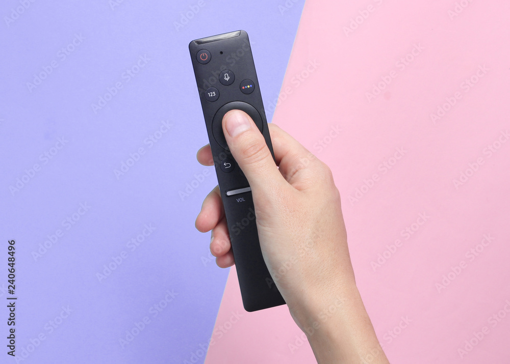 Female hand holds the TV remote on a pink purple pastel background. Top View. Female hand holds the TV remote on a pink purple pastel background. Top View.