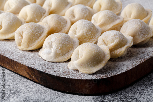 Uncooked russian pelmeni on cutting board and ingredients for homemade pelmeni on white table. Process of making pelmeni, ravioli or dumplings with meat