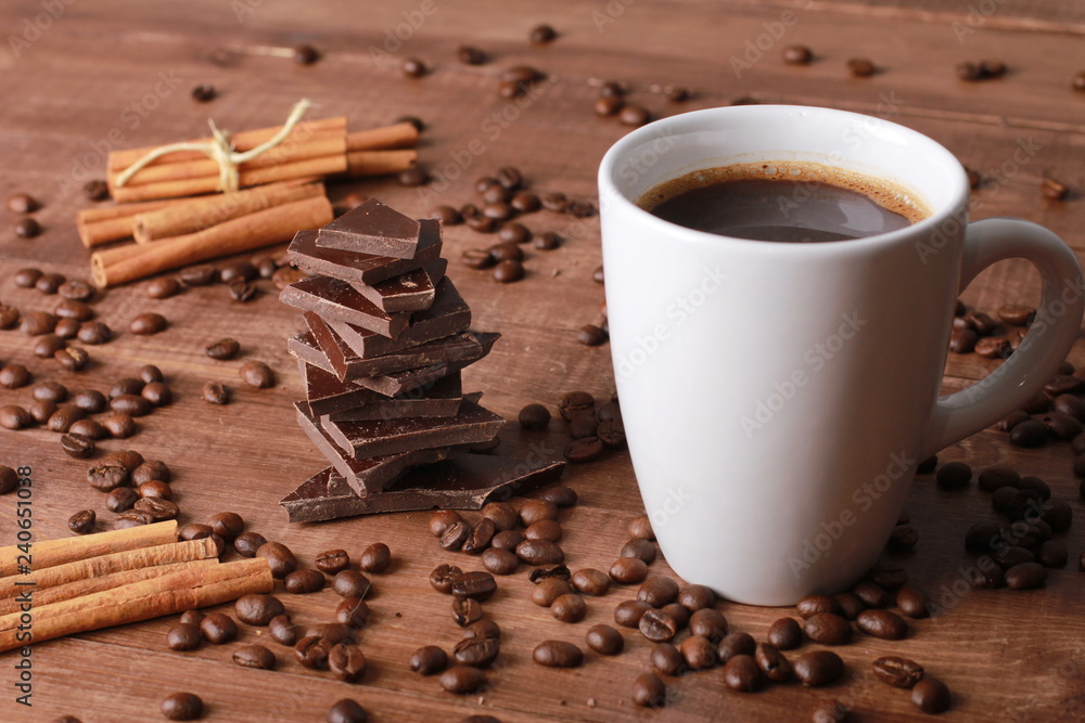 Fototapeta premium Coffee, cinnamon sticks, pieces of chocolate and scattered beans on vintage wooden table. Coffee break concept. White cup, winter drink, espresso, side view