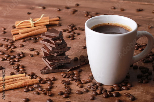 Coffee, cinnamon sticks, pieces of chocolate and scattered beans on vintage wooden table. Coffee break concept. White cup, winter drink, espresso, side view