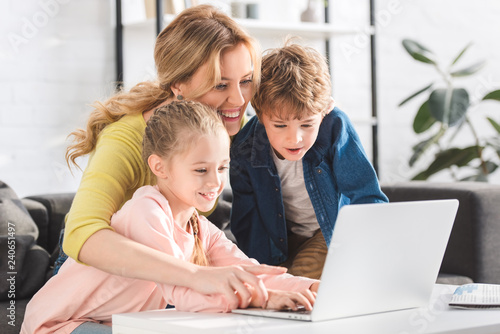 happy mother with adorable smiling kids using laptop together at home
