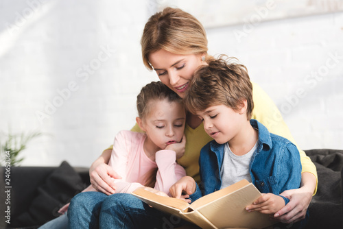 mother with cute little kids sitting on couch and reading book