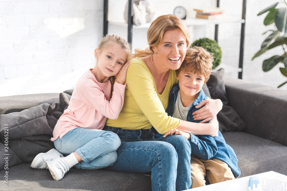 happy mother and adorable little kids sitting on sofa and smiling at camera