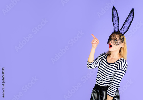 Seductive girl in black lace rabbit mask shows finger blank space for advertising. Beautiful sexy blonde woman in striped clothes in rabbit mask. Halloween, Christmas, New Year, Easter bunny costume.