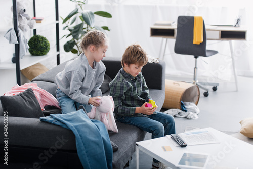 high angle view of siblings sitting on couch and playing with toys at home