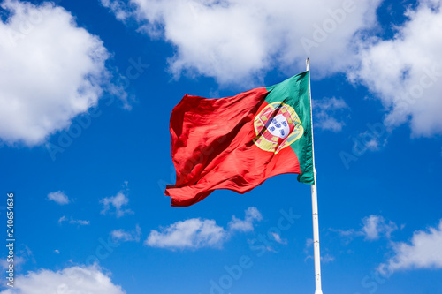 Portuguese national flag waving in the wind against blue sunny sky with white clouds, Portual