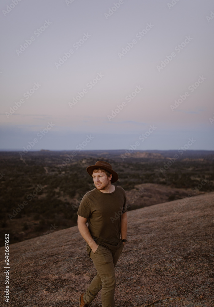 man in hat walking in a desert at sunset