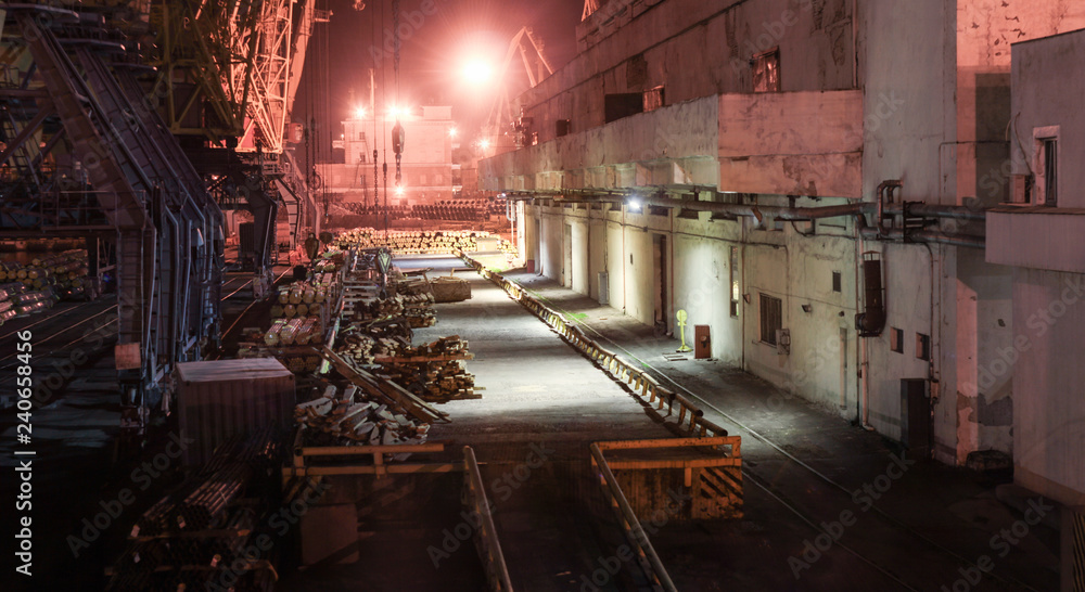 Port warehouse with ramp and cranes at night. Stacked PVC and steel pipe ready for shipment Port warehouse with ramp and cranes at night. Stacked PVC and steel pipe ready for shipment