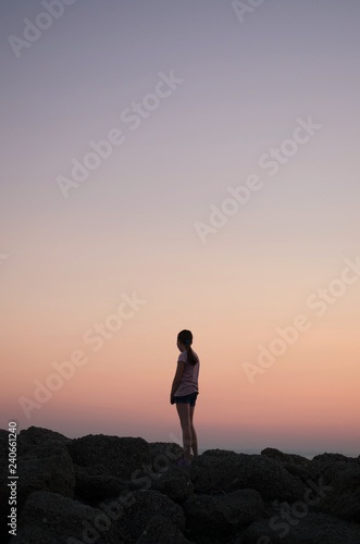 Girl standing on the rocks and watching the sunset