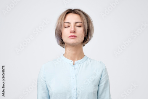 Young european woman in blue shirt closing eyes. No emotion on her face. Dreaming about future.