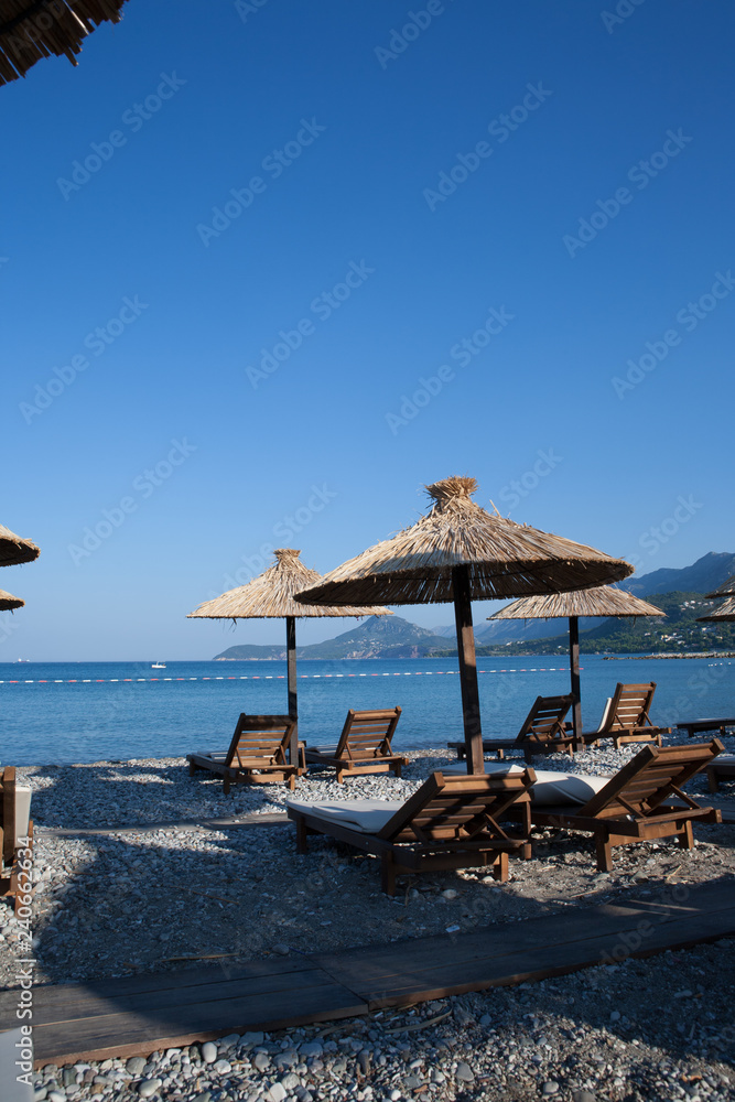Fototapeta premium Bamboo umbrellas and wooden deck chairs on the sandy beach by the sea