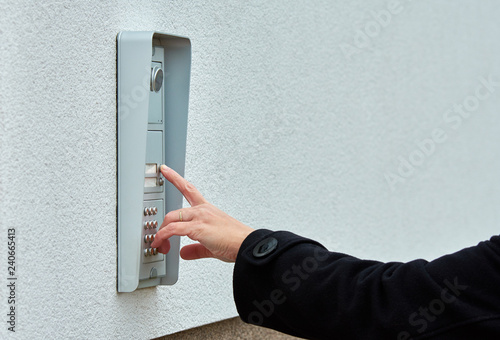 The female hand presses a button doorbell with intercom