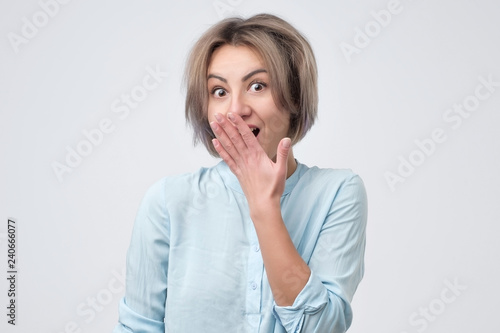 Lovely young woman with shy gesture looking at you on grey background isolated. Gossip concept.