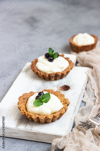Mini tarts (tartlets) with whipped cream or custard and fresh berries served with mint. Homemade dessert. Grey background. Copy space.