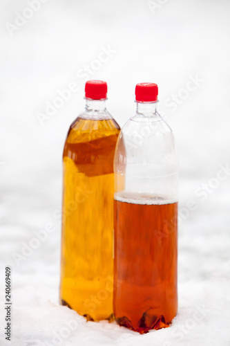 two plastic beer one litre bottles full and half with red caps on white snow background.