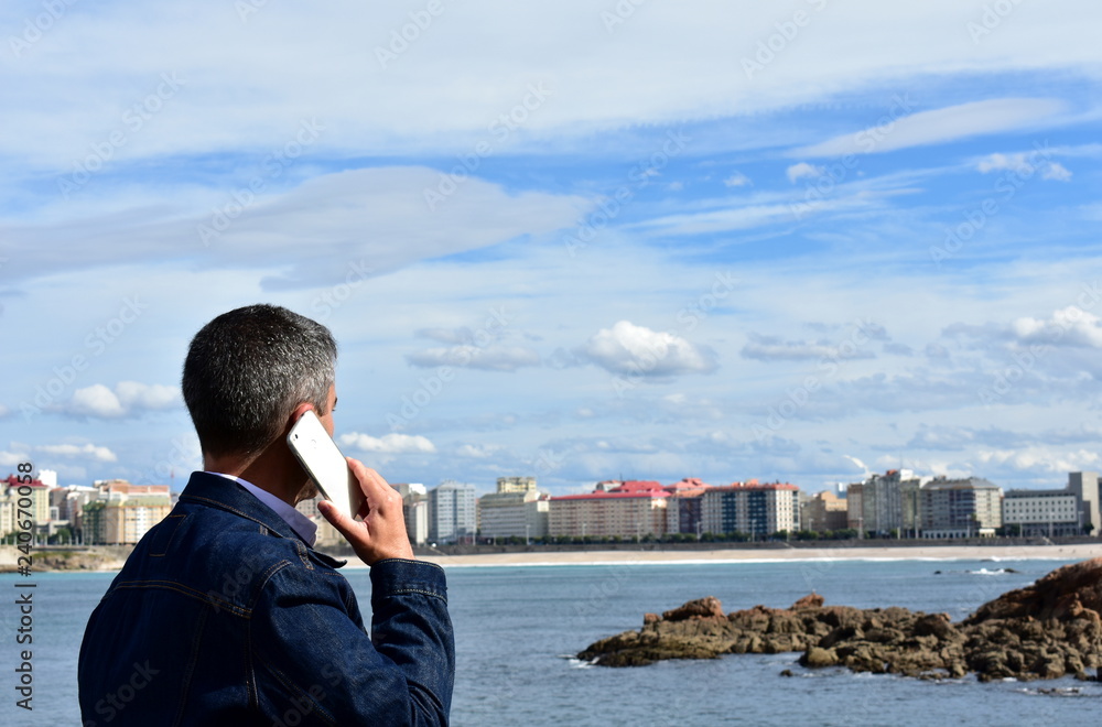 Man talking on a smartphone in a bay. Beach, promenade and city view. Man talking on a smartphone in a bay. Beach, promenade and city view.
