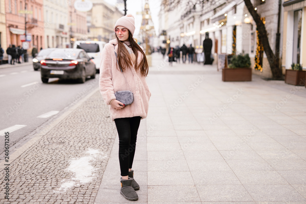 Fototapeta premium Fashion woman walking on the city street, wear pantone color jaket with pink glasses and look to camera. Copy space. - Image