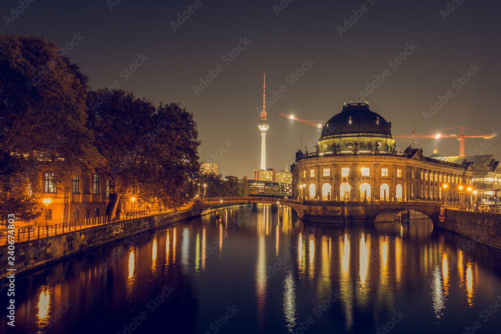 Berlin skyline at night. museum island with river spree and bridges are illuminated in autumn mood. in the background is the TV tower. A path with trees on the river bank. the lights reflect in the wa