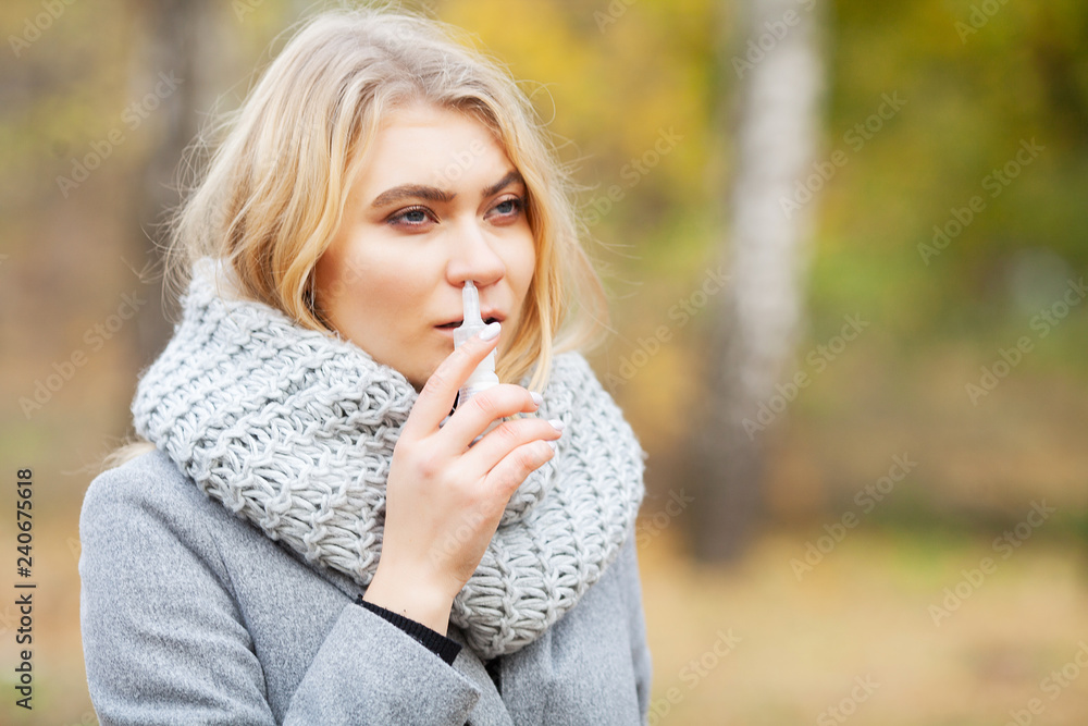 Cold and flu. Young sick woman uses a nose spray at street outside Cold and flu. Young sick woman uses a nose spray at street outside