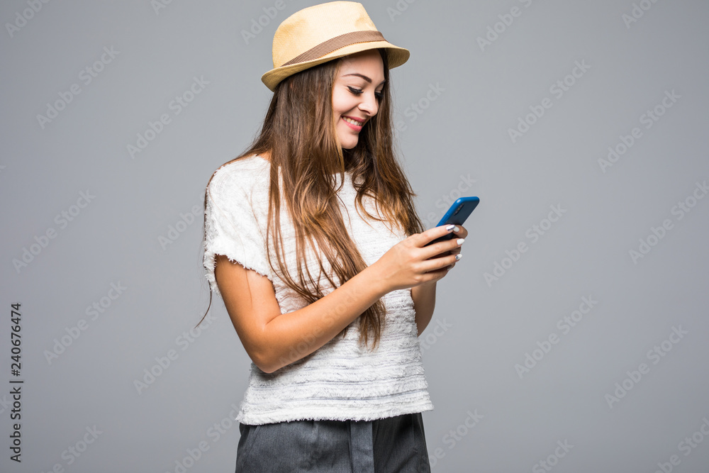 portrait of a smiling young woman in summer hat using mobile phone isolated over gray background portrait of a smiling young woman in summer hat using mobile phone isolated over gray background