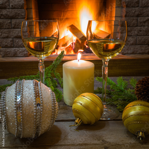 Two glasses of white wine, candle, yellow glass balls, near cozy firepace. photo