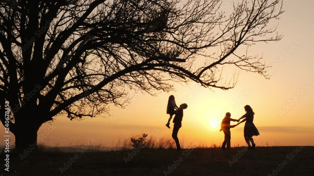Silhouettes of family spending time together in the meadow near during sunset Silhouettes of family spending time together in the meadow near during sunset