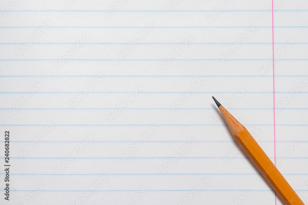 Yellow pencil on the background of a white lined sheet of notebook close-up with copy space Yellow pencil on the background of a white lined sheet of notebook close-up with copy space