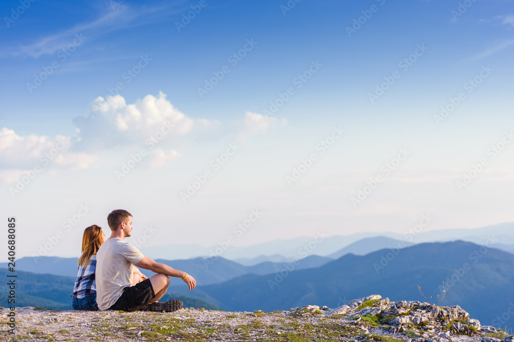 Sitting on the top of the world. A couple enjoying the view on a peak of the mountain having a zen moment, cliff at sunset. Success, winners, zen, tranquility, meditation.