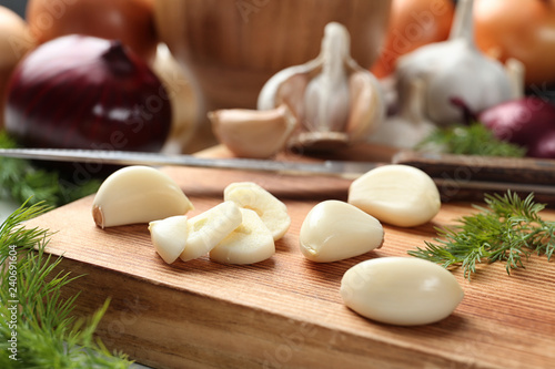 Wooden board with garlic cloves on table, closeup