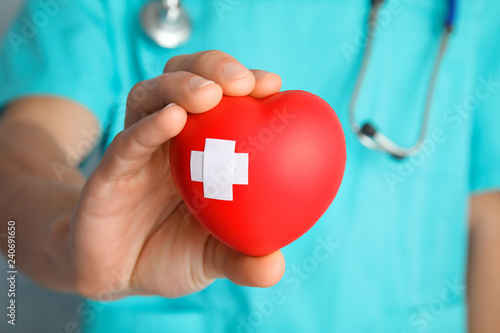 Doctor holding red heart with adhesive plasters, closeup. Cardiology concept