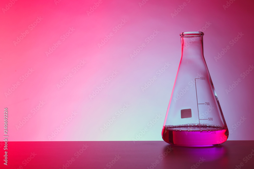 Conical flask with liquid on table against color background. Chemistry laboratory glassware Conical flask with liquid on table against color background. Chemistry laboratory glassware