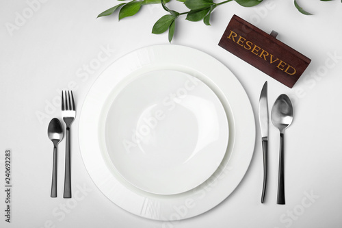 Elegant table setting with RESERVED sign on white background, top view