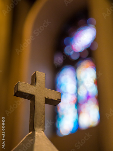 Slika na platnu Cross inside church in foreground with blurry stained glass behind