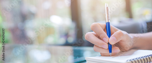 Woman writing on a notebook with a pen in the office.Web banner.