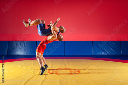 The concept of fair wrestling. Two greco-roman  wrestlers in red and blue uniform wrestling   on a yellow wrestling carpet in the gym