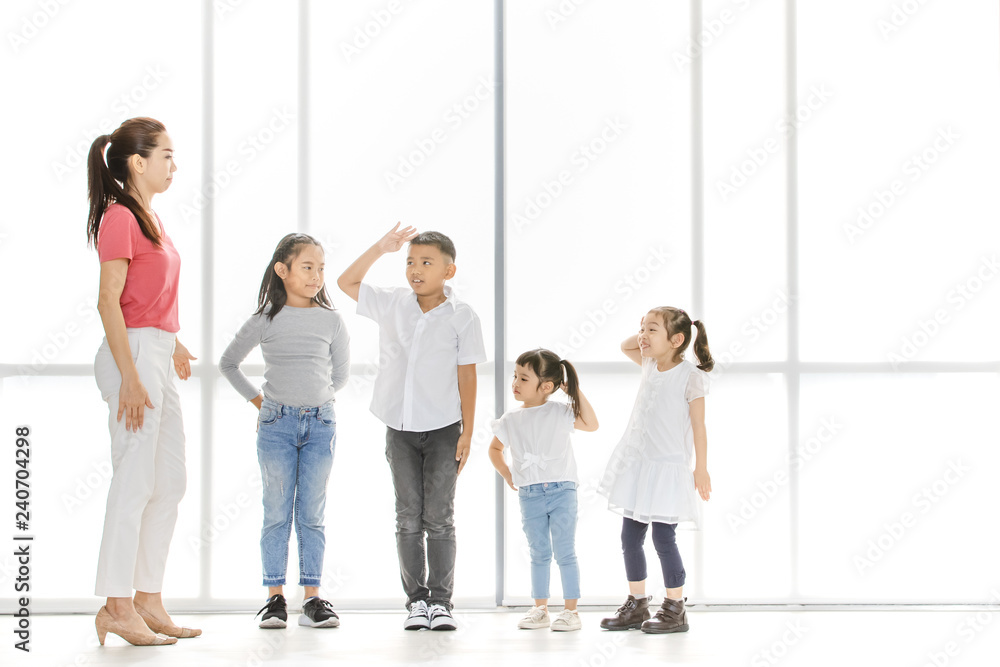 Asian woman and little Asian boy raise their one's hand among Asian kids in front of big white window.
