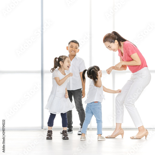 Asian woman in pink shirt teach Asian boy and girls to move their body, they laugh and stand in front of big white window.