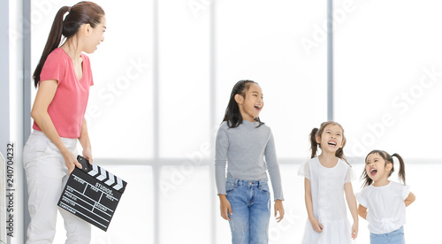 Asian woman in pink shirt Asian use clapper board in front of Asian boy and girls, they stand in front of big white window.