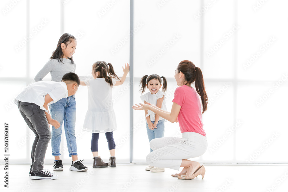 Asian woman in pink shirt playing something with Asian boy ans girls, they stand in front of big white window. Asian woman in pink shirt playing something with Asian boy ans girls, they stand in front of big white window.